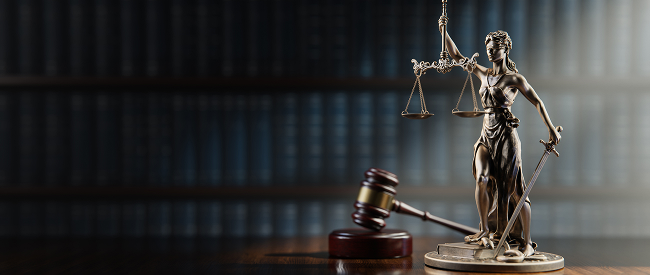 Photograph of a gavel and Themis, the goddess of justice, with a bookshelf in the background.