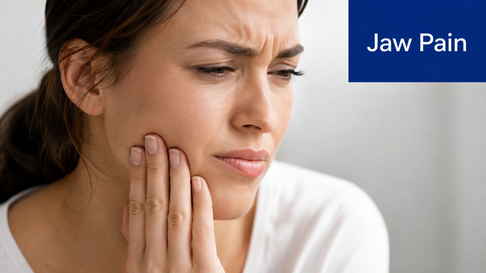 A woman experiencing discomfort while holding her face to represent symptoms of jaw pain.