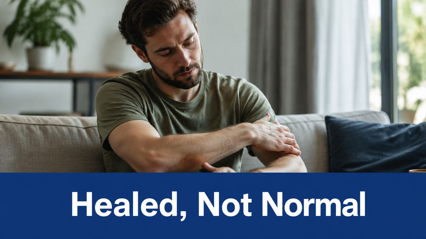 A man sits on a couch touching his elbow, representing recovery from a radial neck fracture.